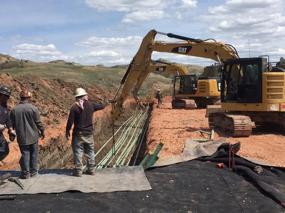 Eaton Construction crew in hard hats laying multiple flowlines in a trench beside CAT excavators